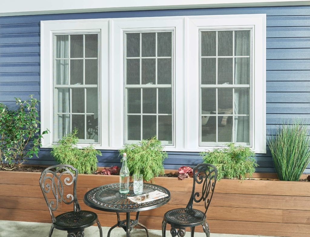 A wrought iron outdoor patio set placed in front of a blue house with white windows and landscaping.