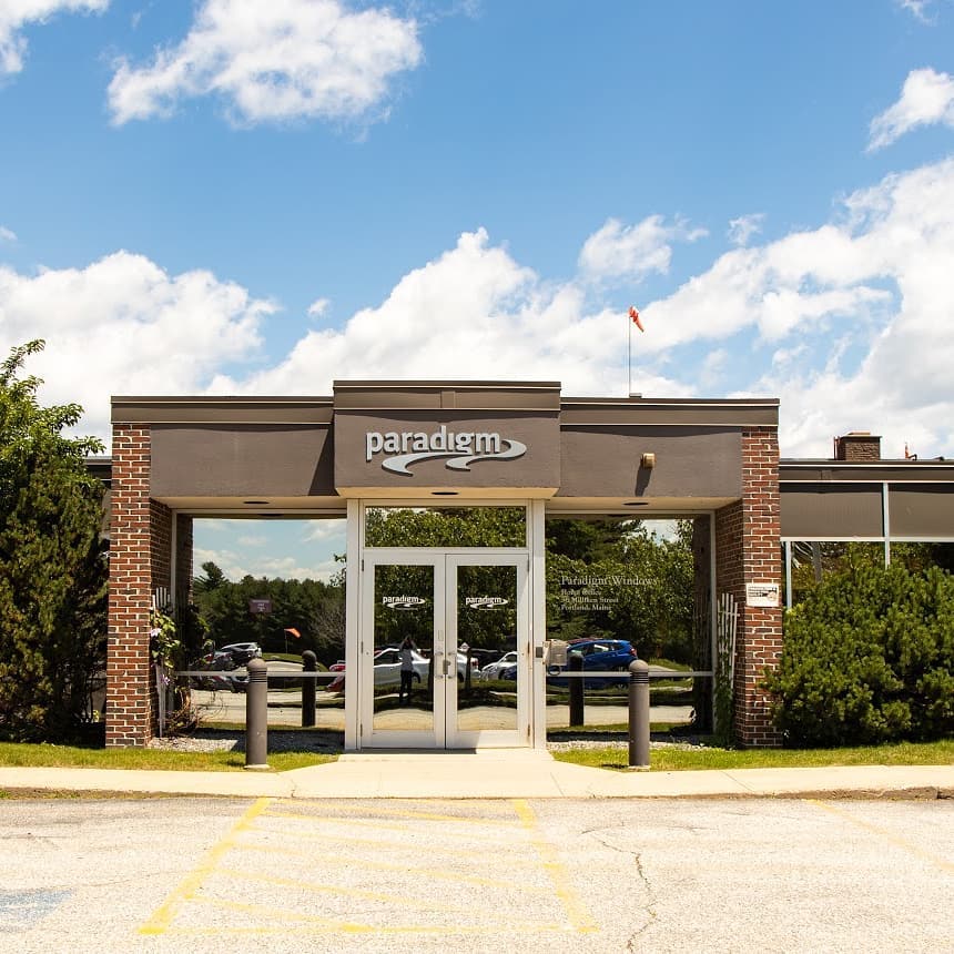 Alt text: Commercial building with “Paradigm” sign in white, a brick exterior and reflective glass doors and windows.