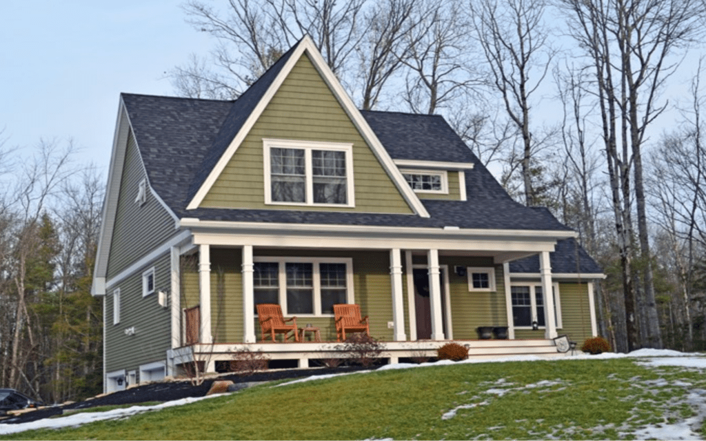 A house with green siding and white trim sitting on top of a snowy hill.