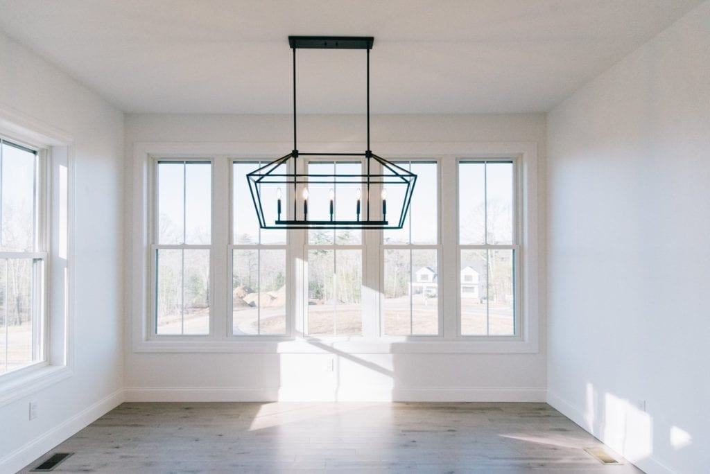 A well-lit empty room with two walls of windows, wood floors and geometrical light fixture.