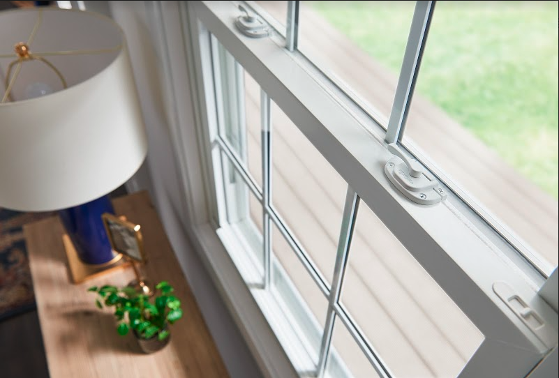 A close up of a white double hung window behind a wooden table with a blue lamp and a plant.