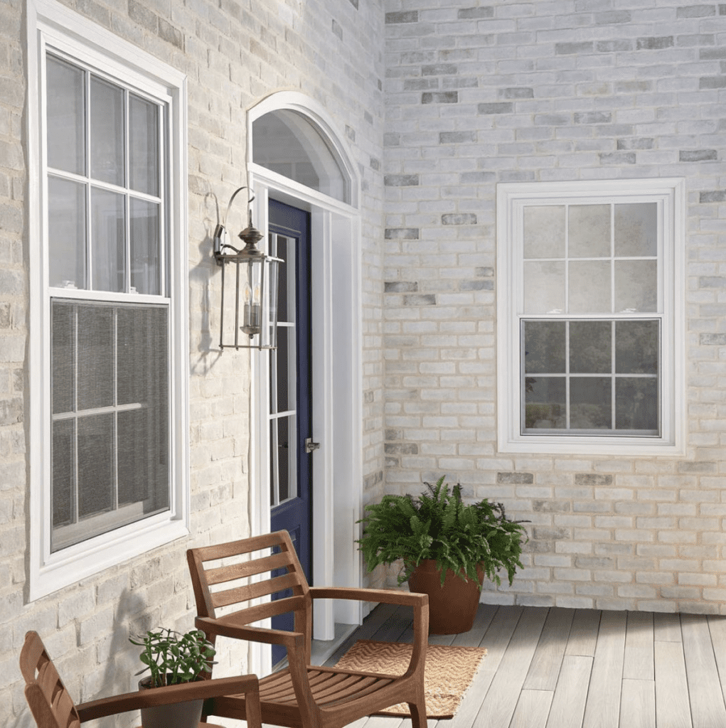 White and grey toned brick home exterior with a dark blue door, two windows and outdoor chairs.