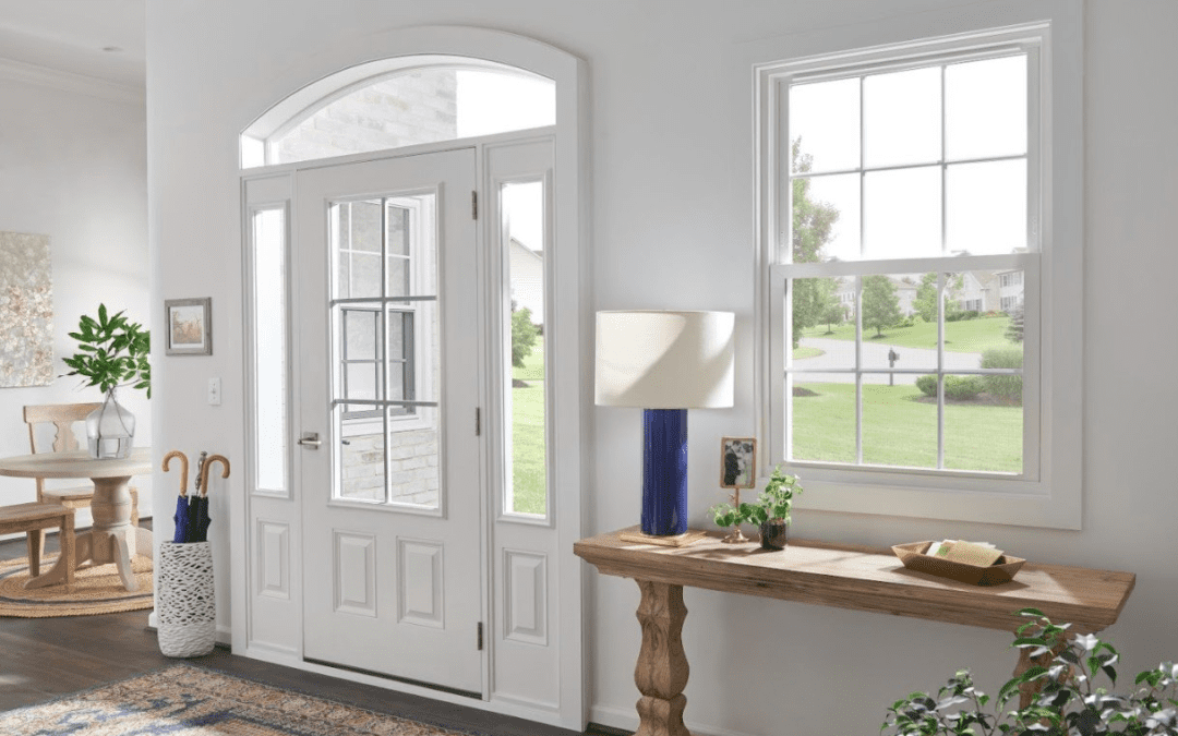 View of a white front door and entry windows from inside the home surrounded by wood flooring, colorful rug and greenery