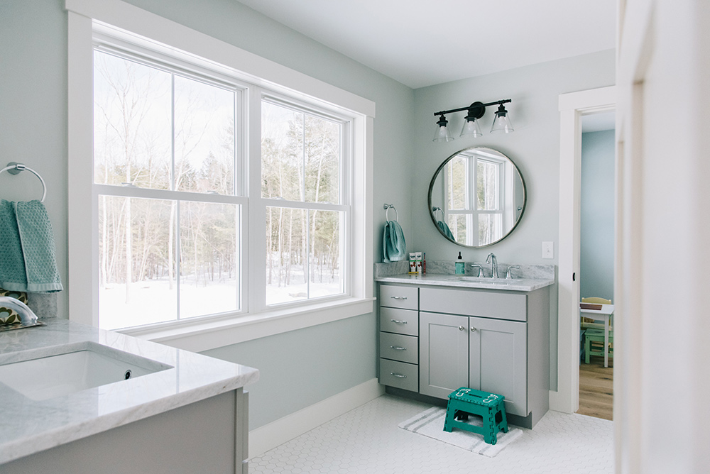A pale blue bathroom with large double hung white windows overlooking a snowy landscape.